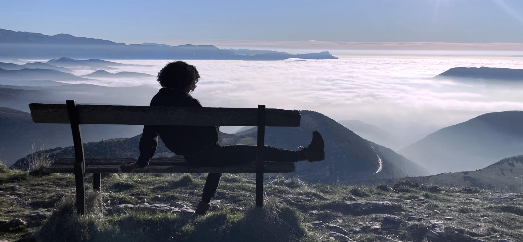Une femme sur un banc contemple un paysage montagneux baigné de brume
